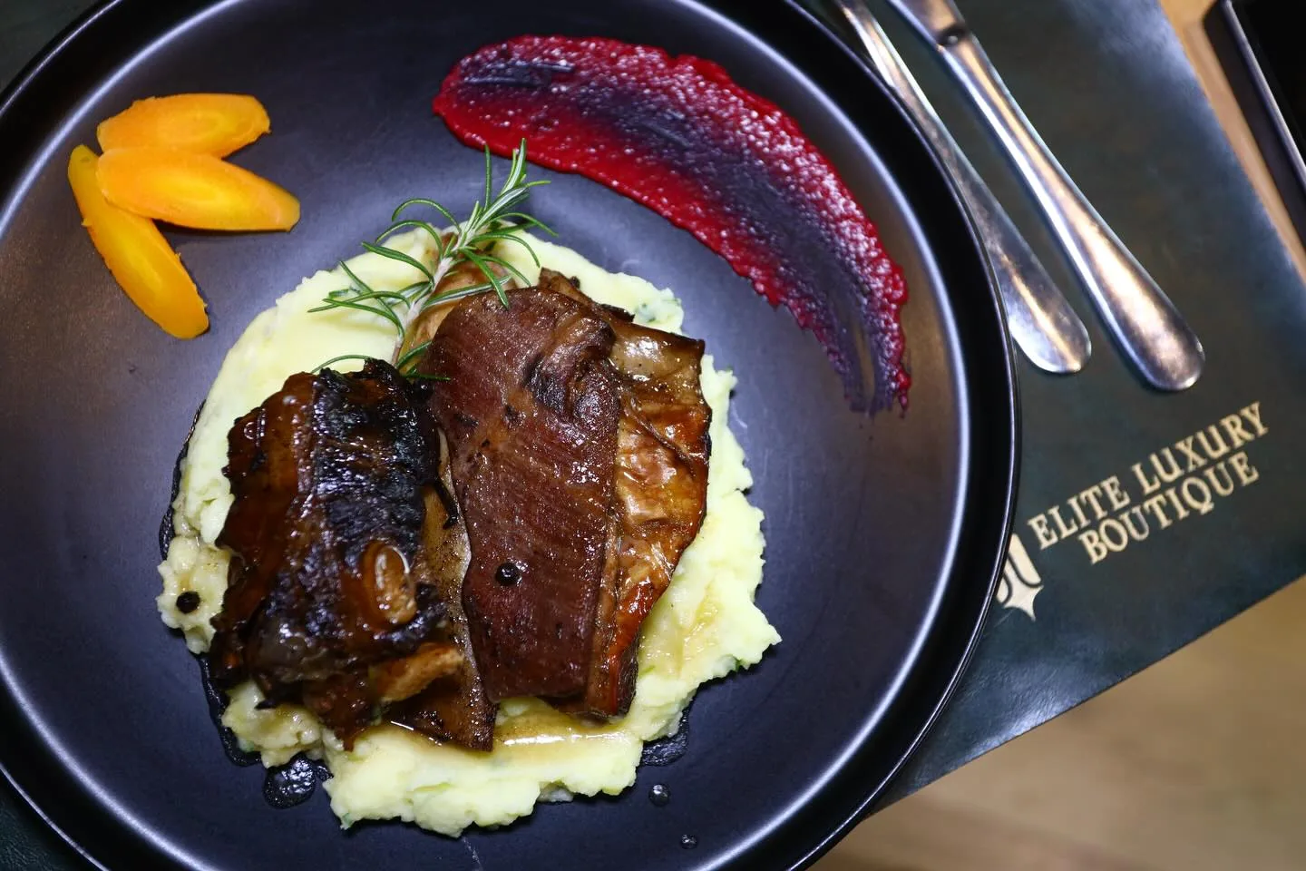 Braised meat on mashed potato with beetroot puree and sliced carrot, served in a black bowl