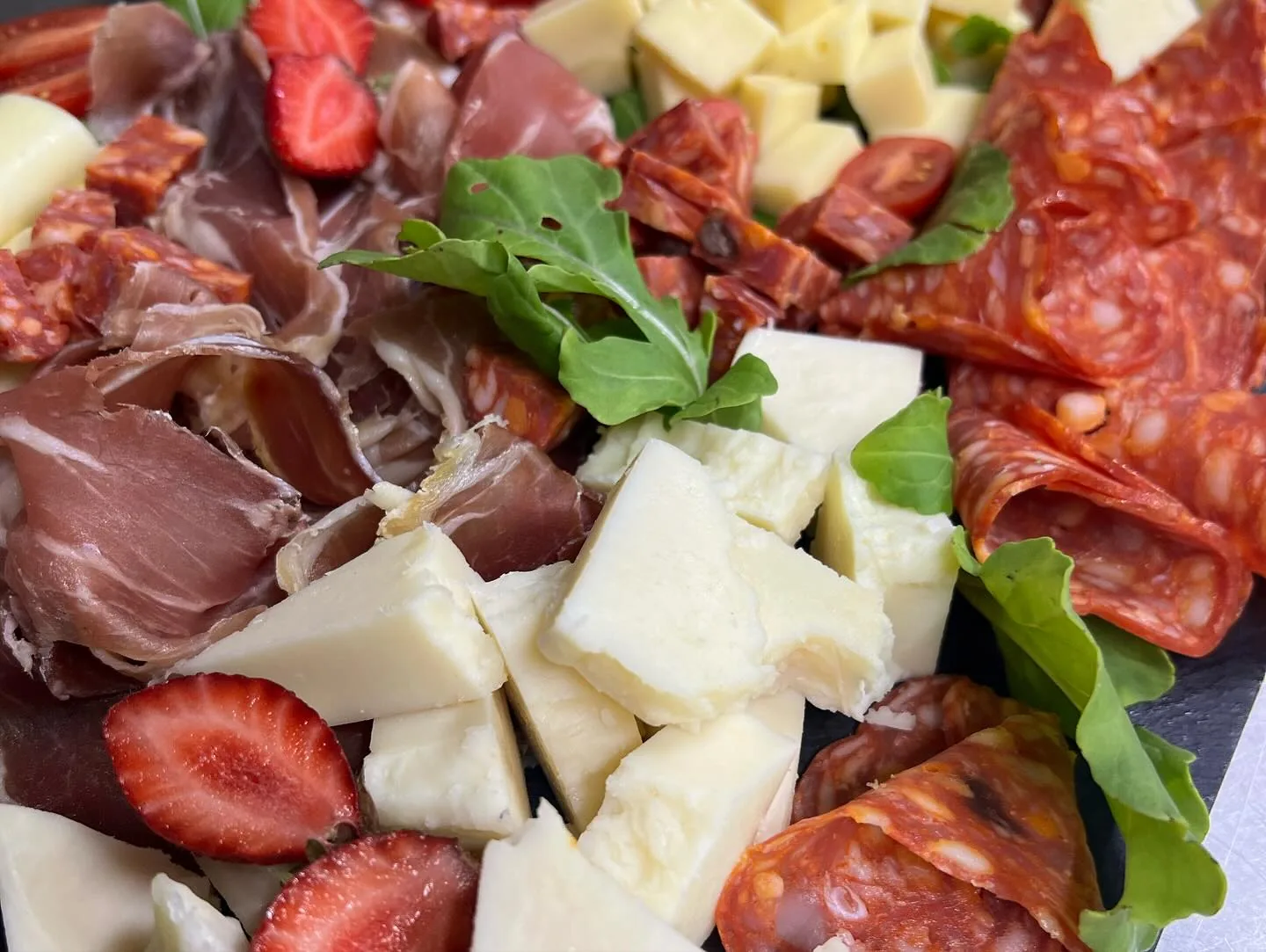 Charcuterie board with cured ham, sliced salami, cubed cheese, strawberries and rocket