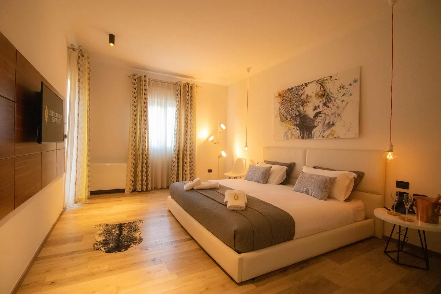 Guest room with a cream upholstered bed, a large portrait canvas above the headboard and a champagne bucket on a side table